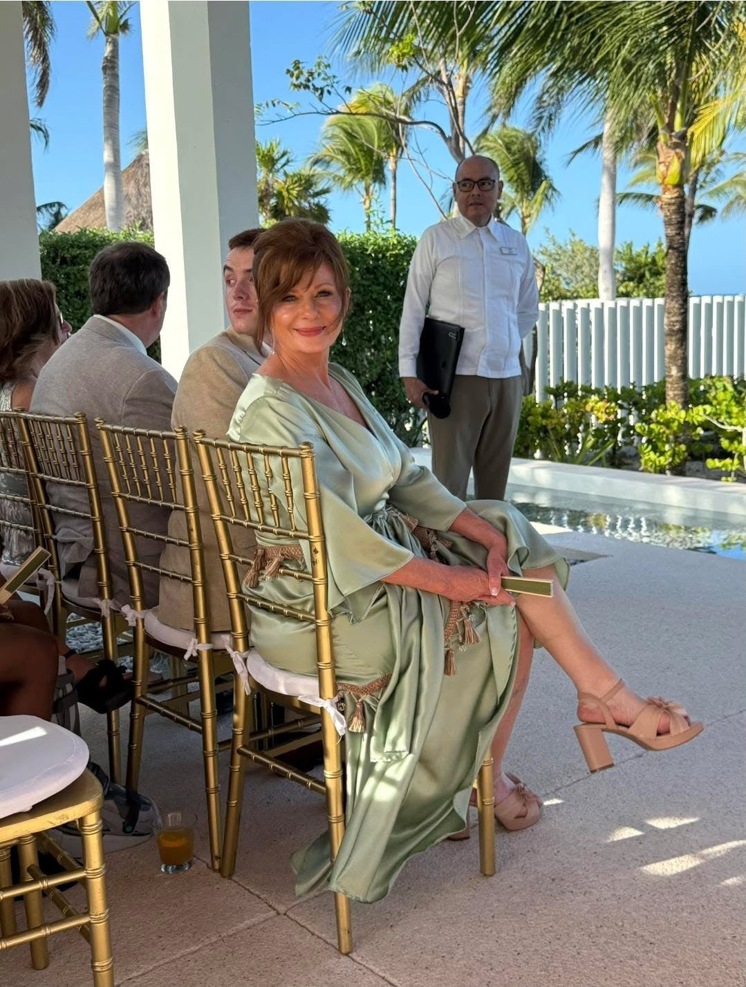 Woman in a green dress sitting on a chair outdoors with palm trees in the background