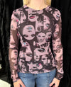 A woman wearing a sheer long-sleeve top with an all-over collage print of stylized faces in pink, black, and gray tones, paired with blue jeans.