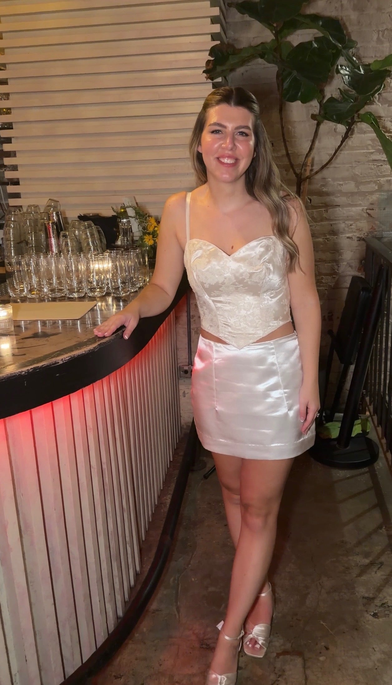Woman in a white dress standing in a bar setting with glasses and decor.