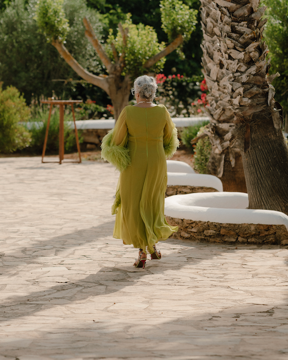 Woman in a green dress with a fur stole walking on a stone path in a garden.